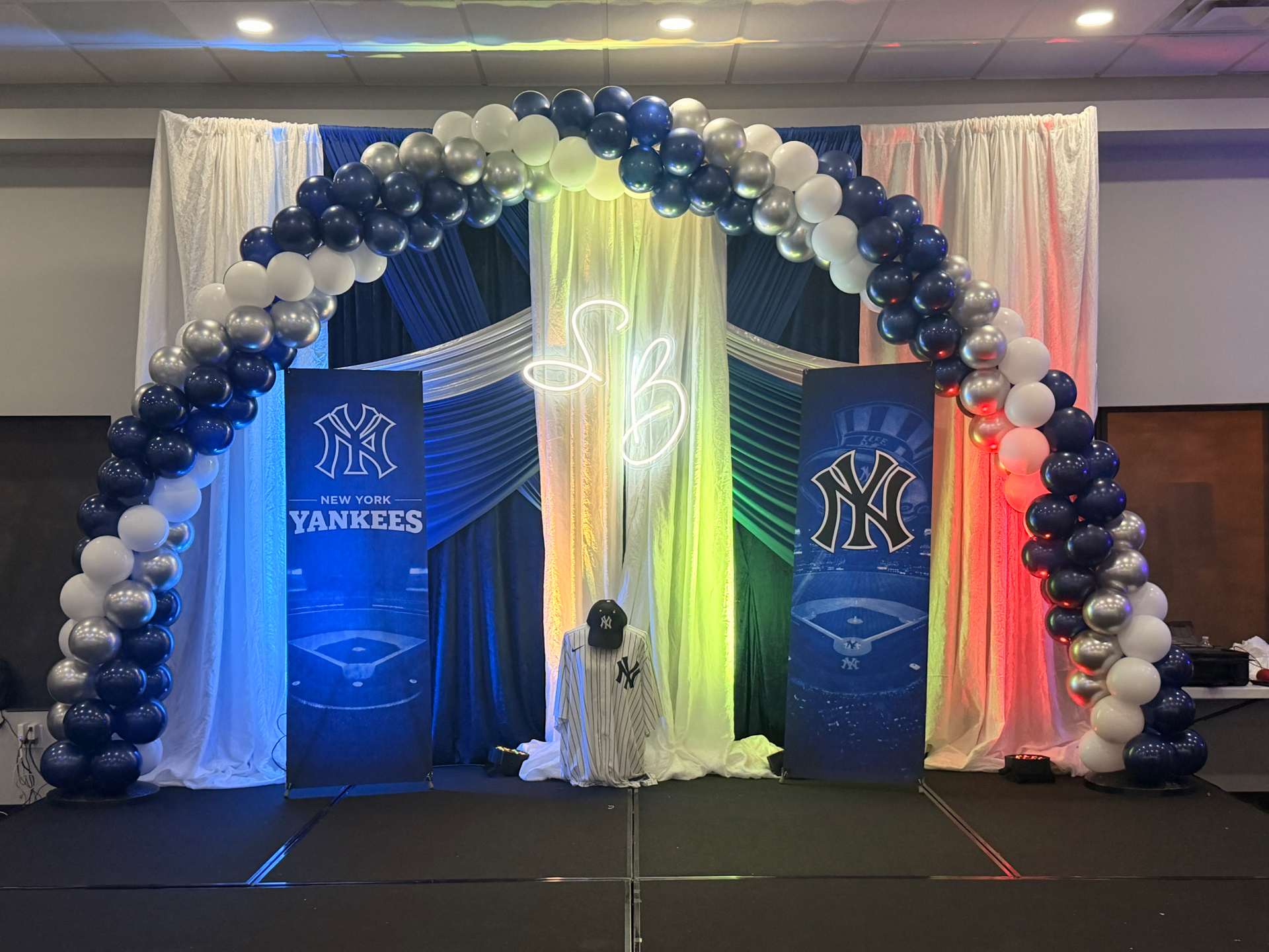 Navy, silver & pearl arch over a lit stage backdrop — Balloon Décor by Good Time Mascots in Columbus, Ohio